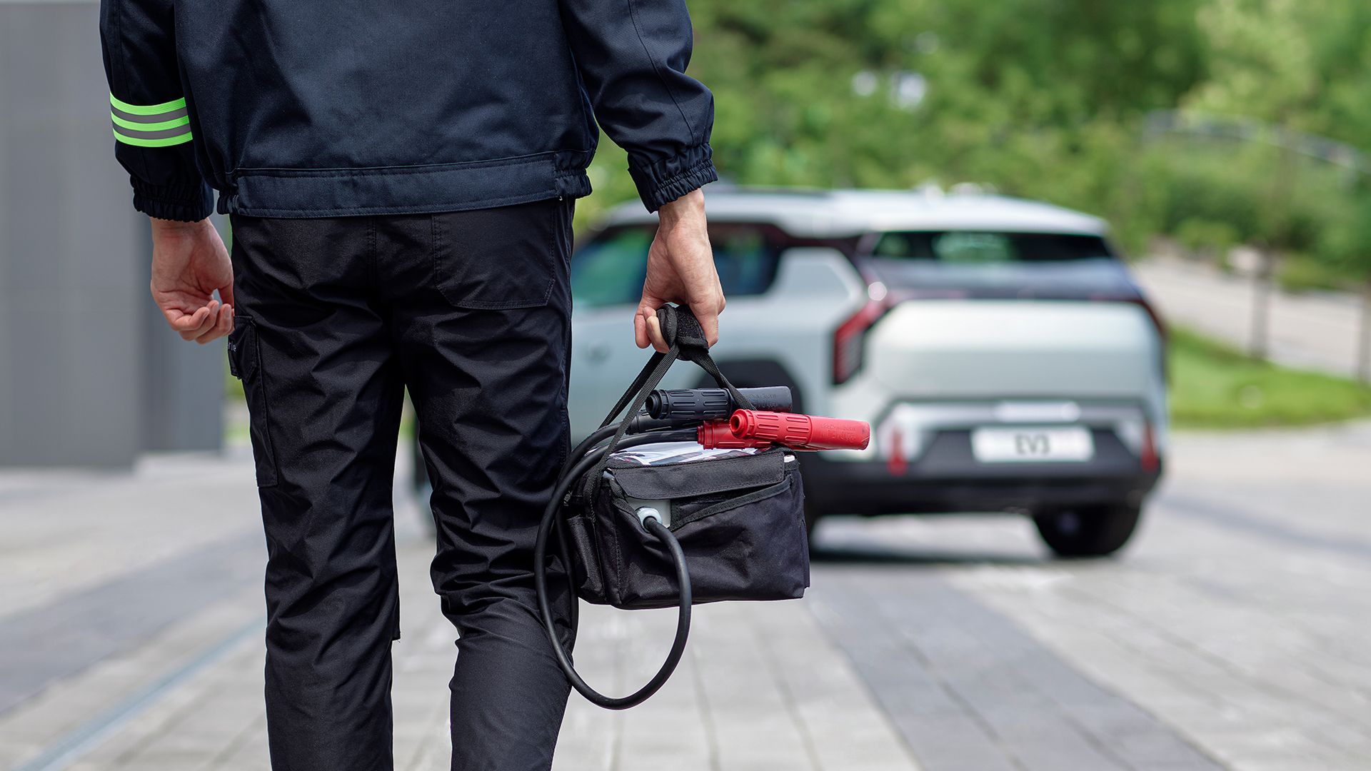 Roadside Assistance technician approaching a parked Kia EV3 with a jump starter kit