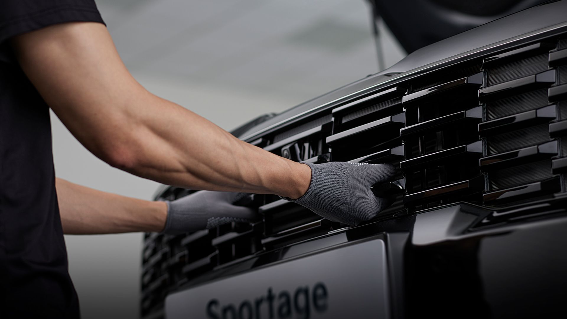 Technician inspecting the front grille of a Kia Sportage HEV during a maintenance check