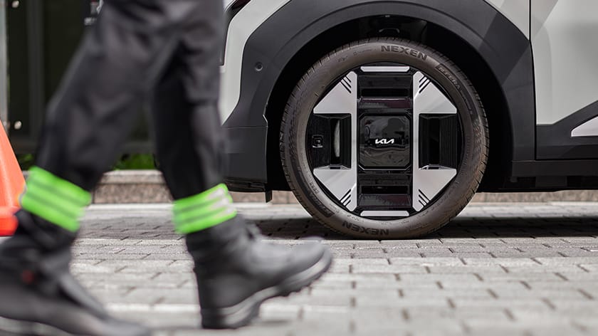 Roadside Assistance technician walking past the front wheel of a parked Kia EV3