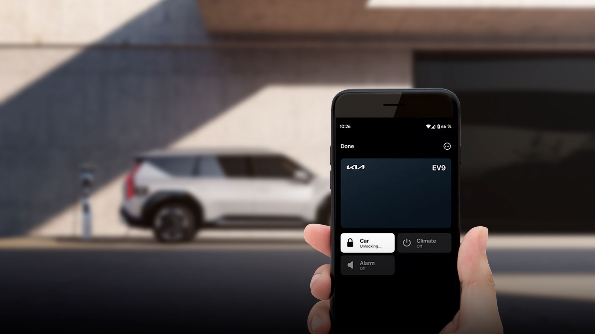 Hand holding a smartphone using a digital key to unlock a parked Kia EV9
