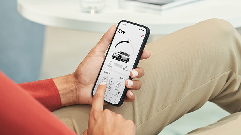 Hand holding a smartphone using the Kia Connect app to start the vehicle and control climate settings