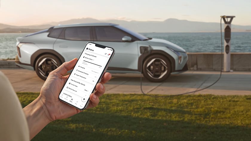 Hand holding a smartphone using the Kia Connect app to control charging while the vehicle is plugged in