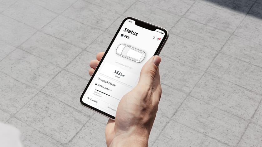 Hand holding a smartphone showing the Kia Connect app displaying driving range and battery status