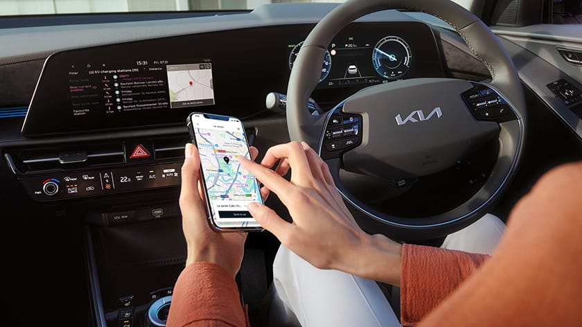 Hand holding a smartphone sending a map destination from the Kia Connect app to the vehicle navigation system