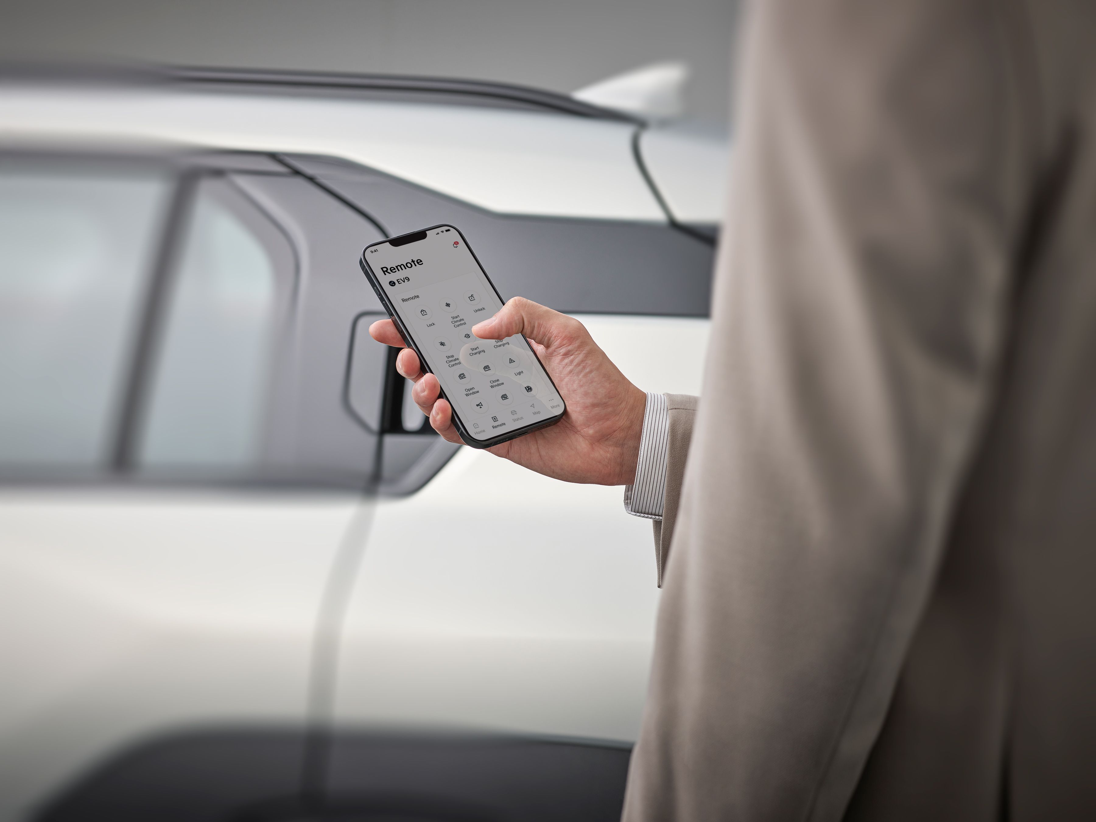 Hand holding a smartphone using the Kia Connect app to control vehicle features beside the parked car