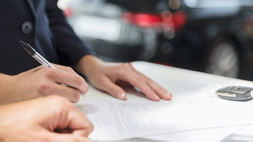 Close-up of two people signing the papers at the car dealership 