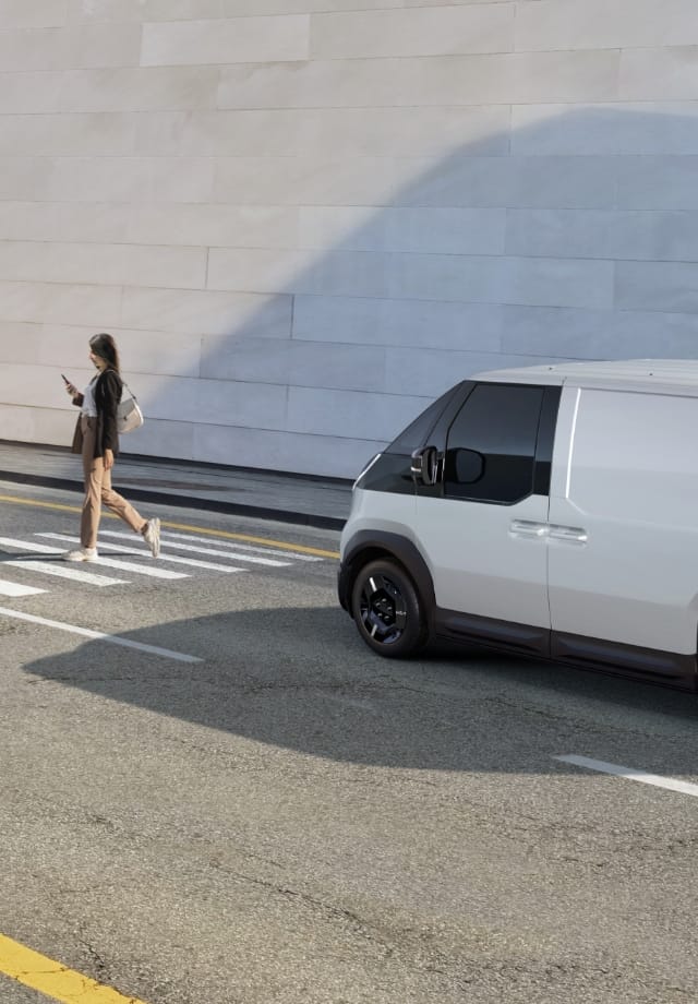 The Kia PV5 Cargo stopped at crosswalk while a pedestrian walks by