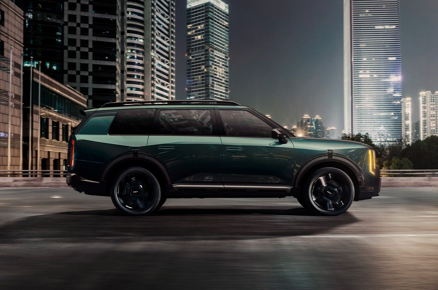 2027 Kia Telluride Hybrid in green driving on an urban highway, with buildings in the background. The image highlights the SUV’s sleek design.