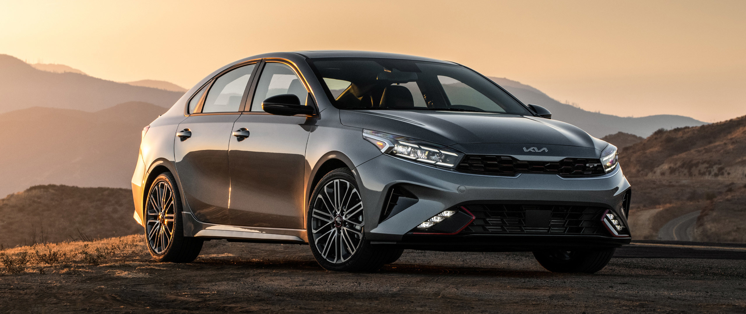 2023 Kia Forte With Exterior Accents Parked In Front Of Mountains At Sunset - Three-Quarter View