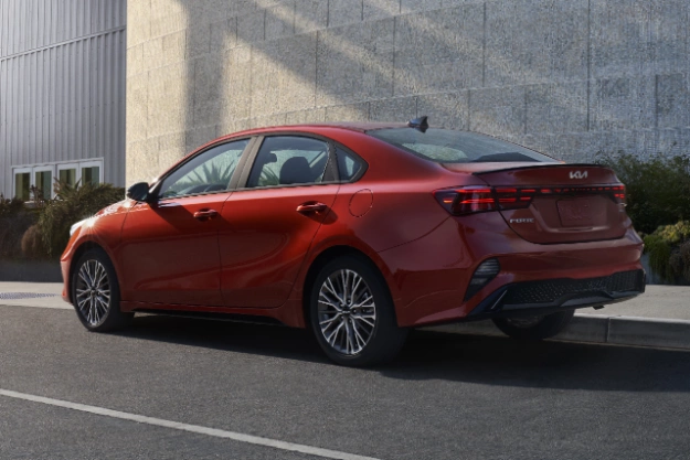2024 Kia Forte in red parked in front of an urban exterior, three-quarters rear view