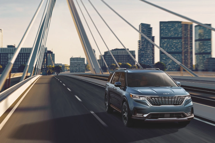 2023 Kia Carnival Driving Across A Bridge At Sunset Front View