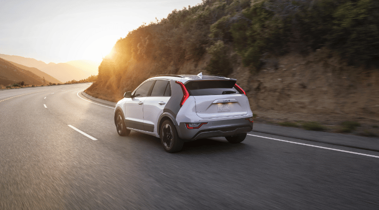 Rear end view of a 2024 Kia Niro EV driving on mountain road towards the sunset. 