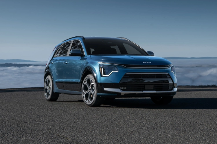 2023 Niro PHEV in blue, parked on overlook with clouds and the ocean in the background.