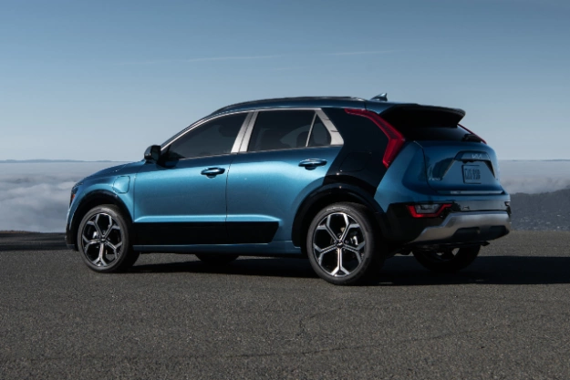 2023 Niro PHEV in blue, rear-view action shot while driving down a forest road.