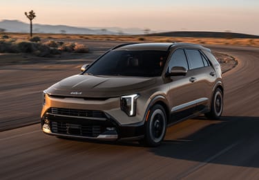Dynamic front driver's-side angle view of the 2027 Kia Niro Hybrid electric SUV in bronze brown driving quickly around a curve in a road in the desert. It looks impressive and powerful.