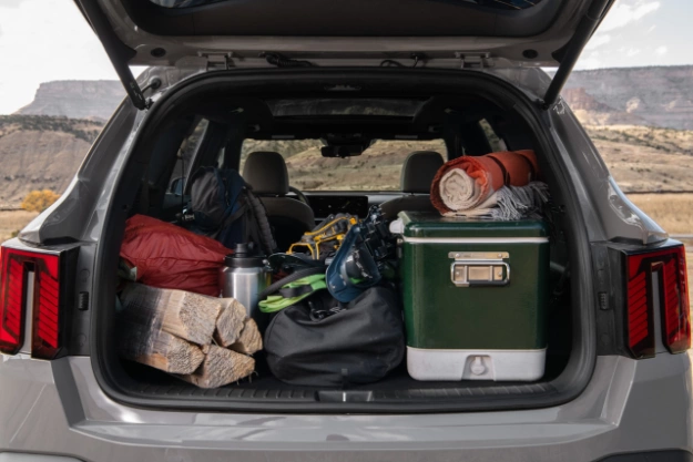Vista trasera del Kia Sorento 2024 en gris con el baúl abierto lleno de equipamiento para campamento, que incluye una gran hielera, mantas, un paquete de madera, bolsas de dormir, mochilas y zapatos para la nieve