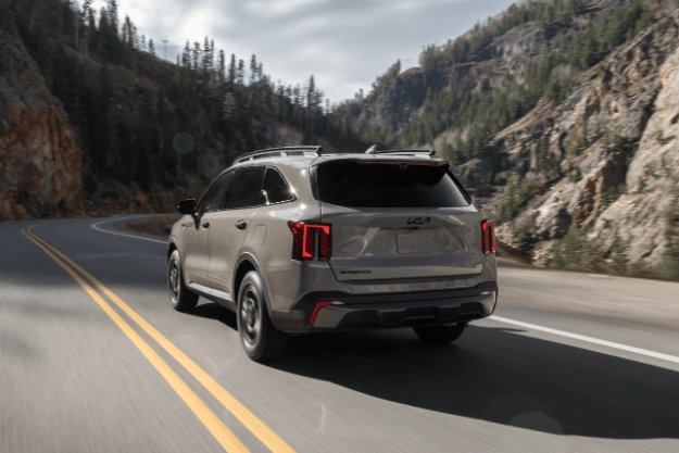 2025 Kia Sorento, three-quarter back view, driving down a winding road in the mountains