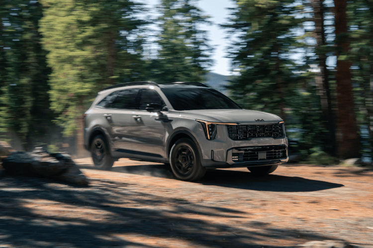 2025 Kia Sorento, three-quarter front view, driving on a dirt road through trees
