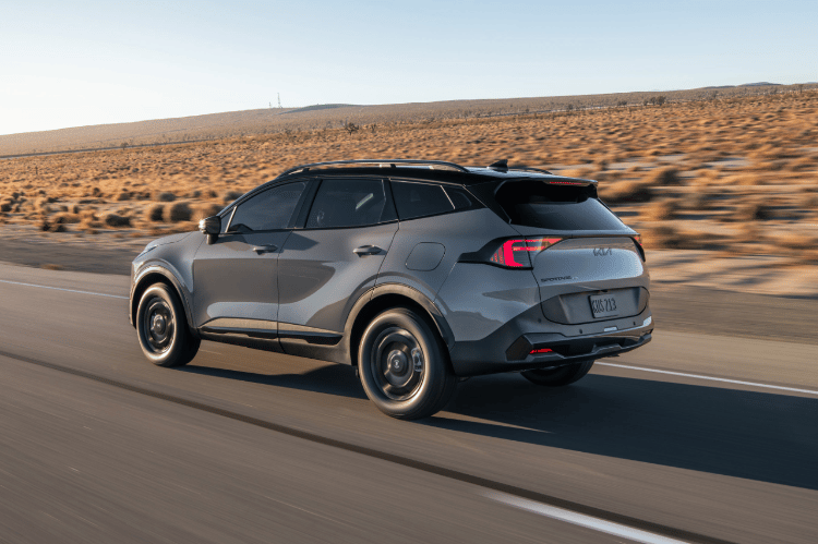 Vehículo Sportage 2026 en vista tres cuartos trasera, circulando por un camino desértico