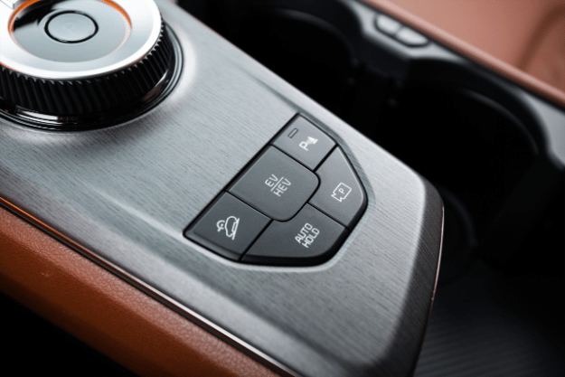 Interior del vehículo Sportage 2026, vista ampliada de la consola central con el dial de cambio de marchas rotatorio y los botones de asistencia de estacionamiento