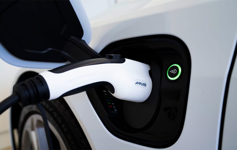 Close-up shot of the black and white Ampure Go portable charger for hybrid electric vehicles, capable of delivering Level 1 and Level 2 charging using standard 120V or 240V outlets, plugged into the open socket of a white Kia vehicle, with a green ring indicating active charging status.