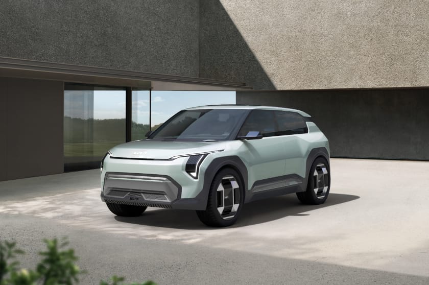 Light green Kia EV3 concept vehicle in a three-quarter front view, parked in front of a modern building.