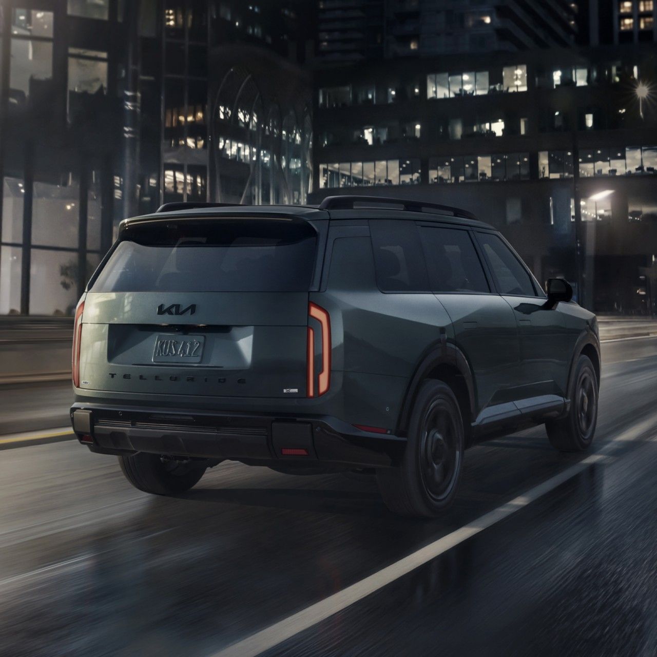 2027 Kia Telluride Hybrid in green driving on an urban highway, with buildings in the background. The image highlights the SUV’s exterior trunk area and sleek design.