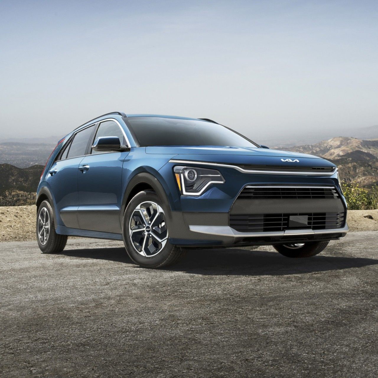 2026 Kia Niro Hybrid EX in blue, three-quarter front view, parked by a cliff in the mountains