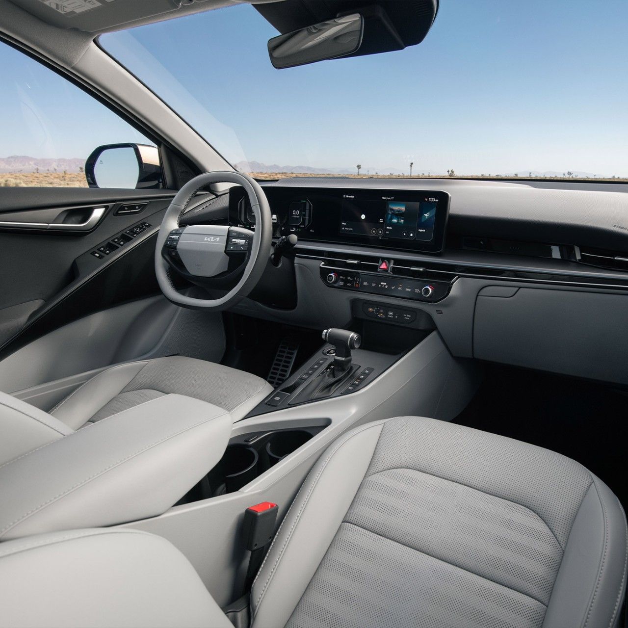 Interior view of the 2027 Kia Niro Hybrid SUV showcasing the steering wheel, grey front seats, center console, and dashboard. Desert landscape is visible through the windshield.