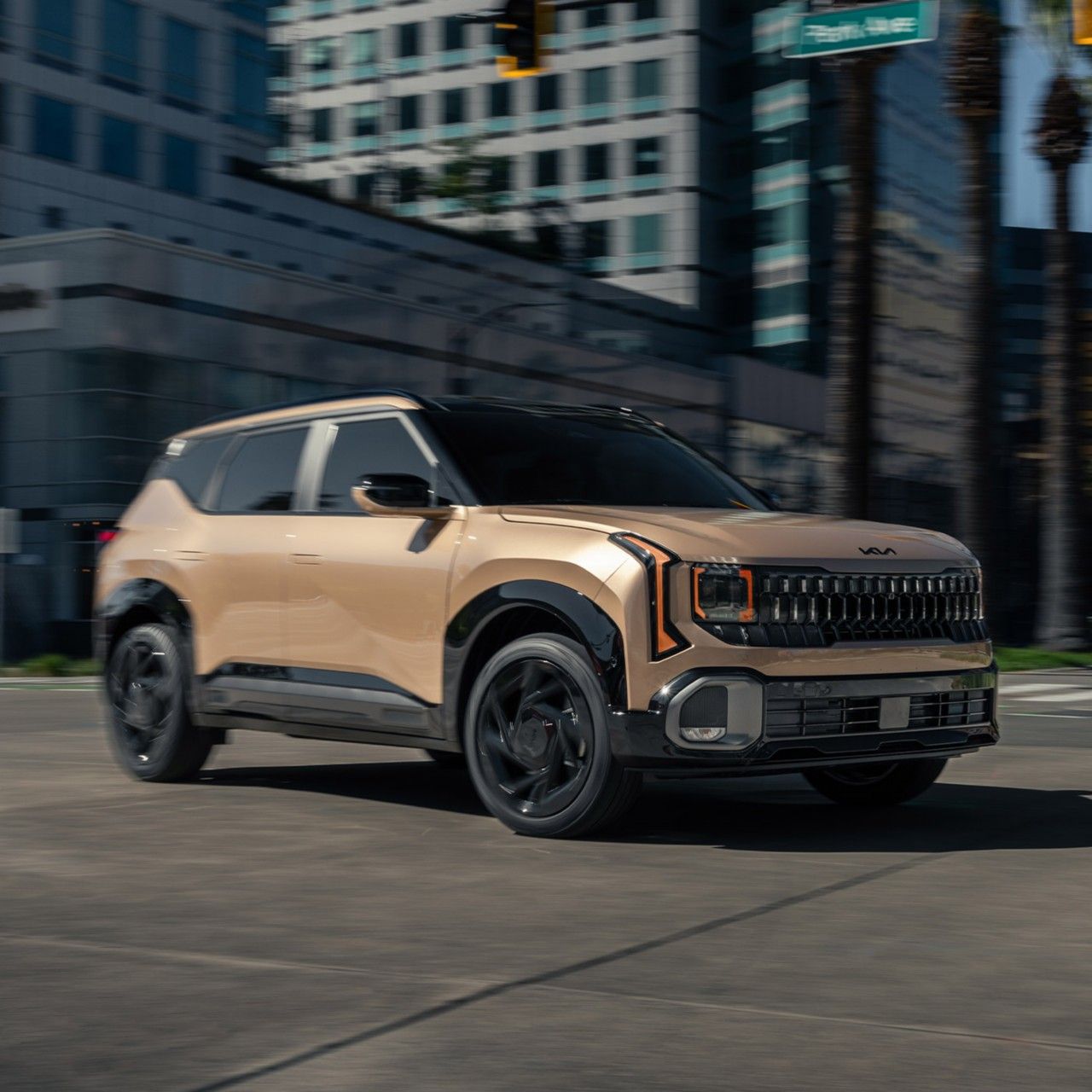 Action shot of the 2027 Kia Seltos SUV in copper-gold color making a turn on Park Ave in an urban environment, showcasing its dynamic contours.