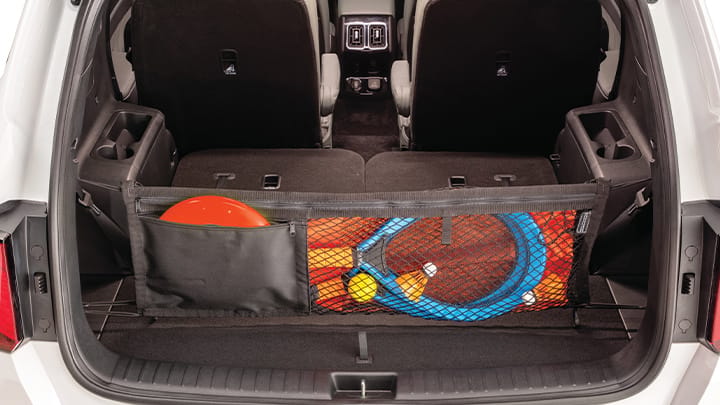 Close-up photo of a Kia vehicle in white with an open trunk showcasing the spacious cargo area. A cargo net accessory is in the trunk and is filled with sports gear.