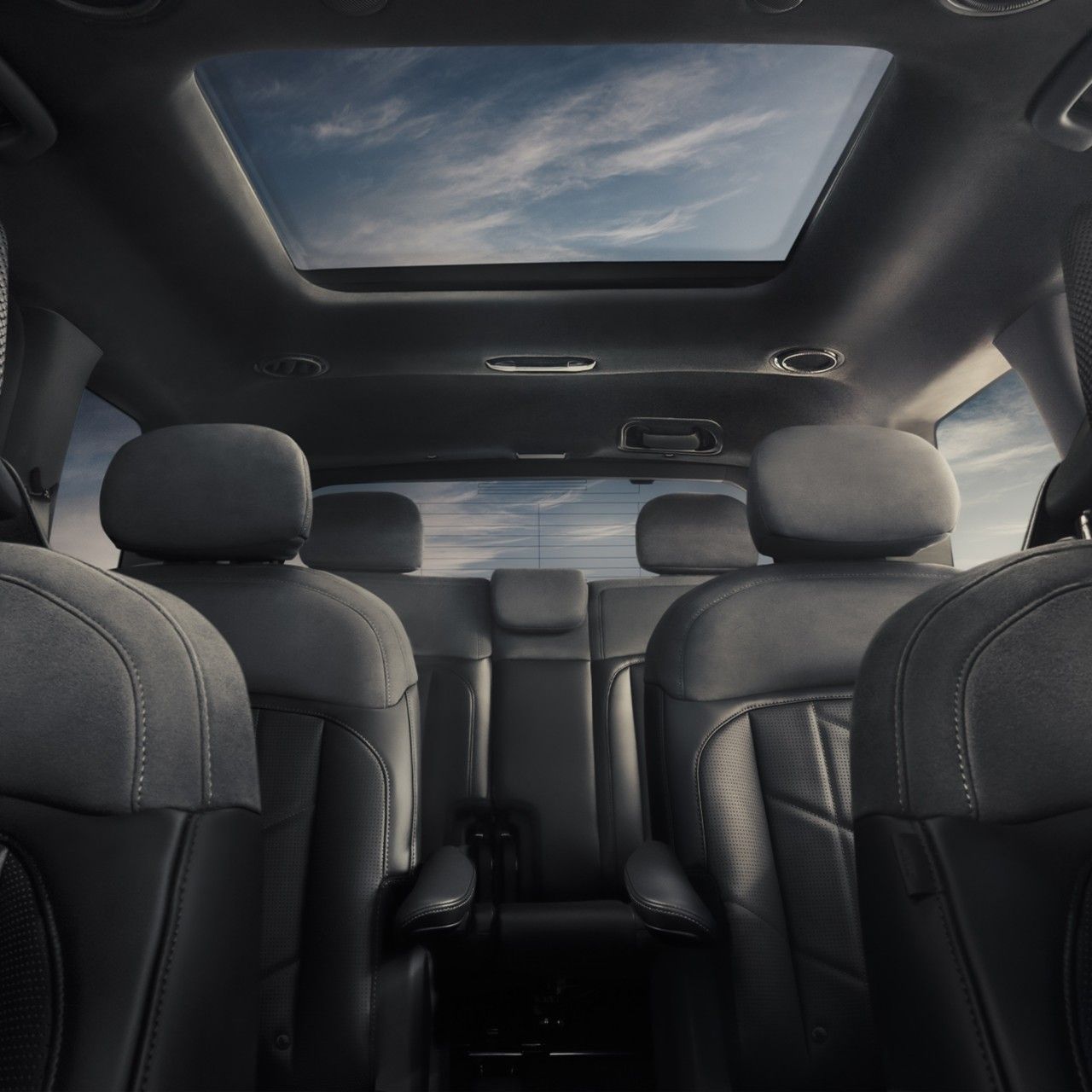 An interior view of the 2027 Kia Telluride featuring black leather seats, three-row seating, and a wide sunroof.  Blue sky and clouds are visible through the windows and panoramic sunroof.