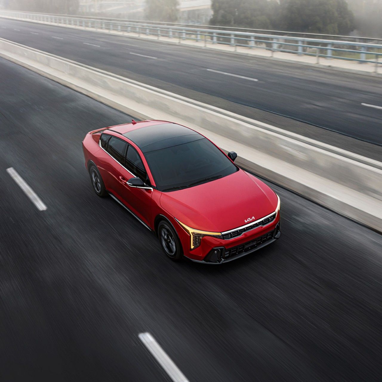Exciting image of the 2026 Kia K4 sedan in red with black and silver highlights, driving quickly over a paved road. The image is meant to inspire a thrilling, limitless feeling.
