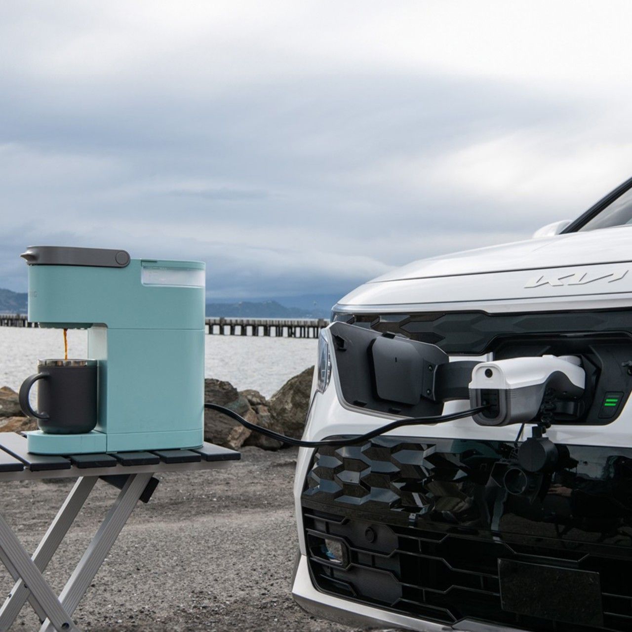 El Kia Niro EV 2026 utiliza el generador de energía a bordo para encender una cafetera en un campamento.