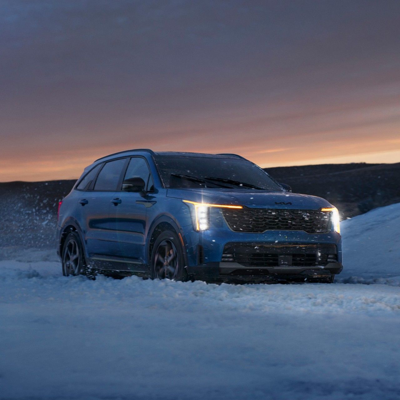 2026 Kia Sorento Hybrid, vista frontal de tres cuartos, con los faros encendidos conduciendo a través de la nieve